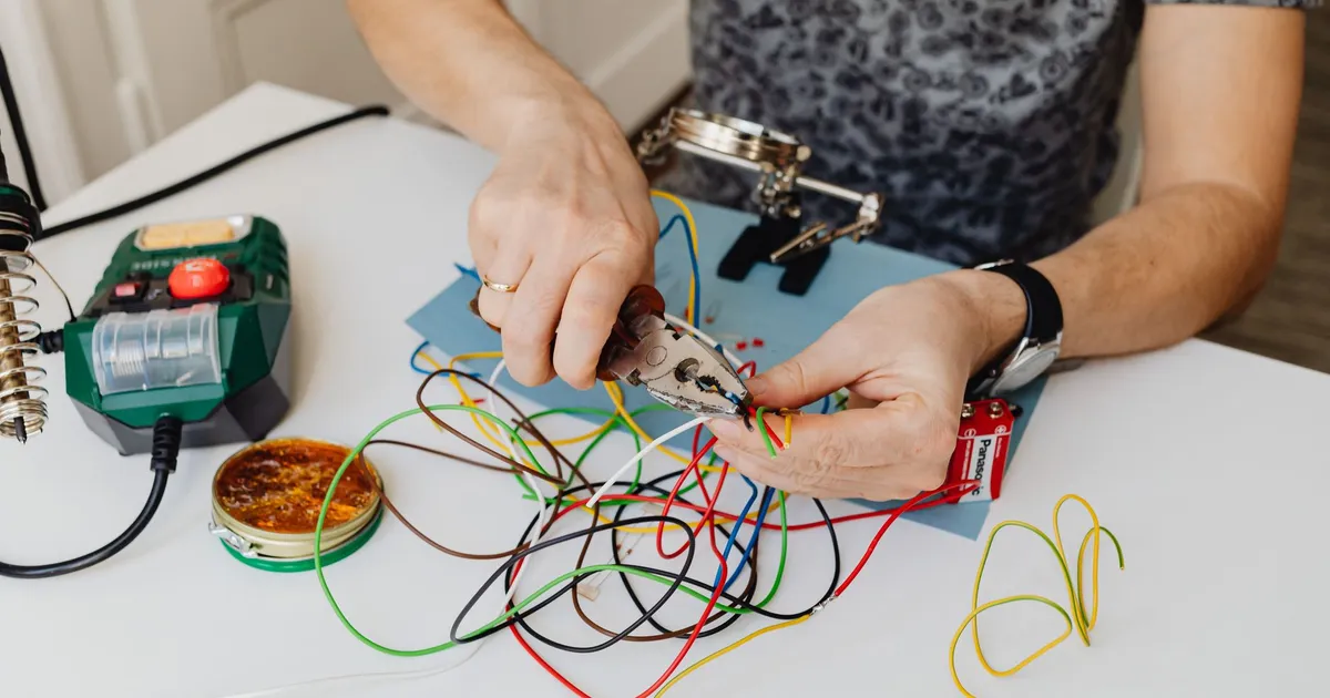 A technician precisely cuts and organizes colorful wires using pliers, showcasing expertise in wiring tasks.
