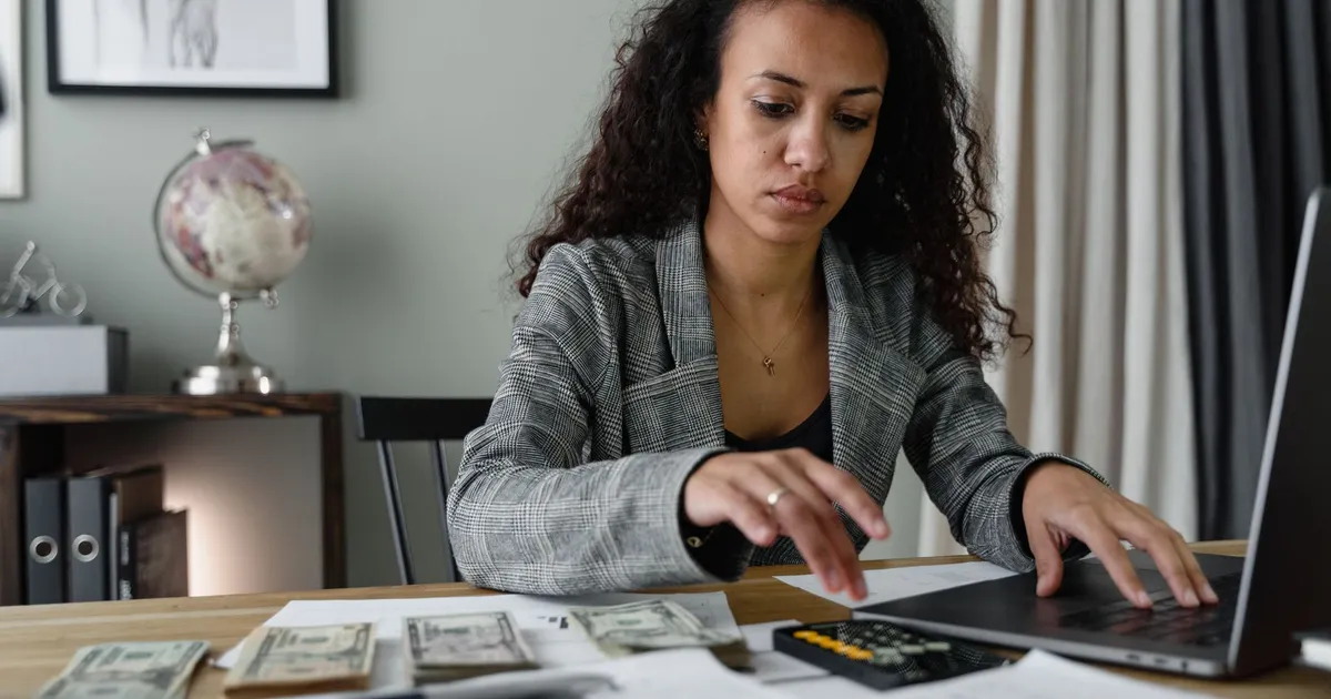 Professional woman analyzing financial documents and counting cash at office desk.