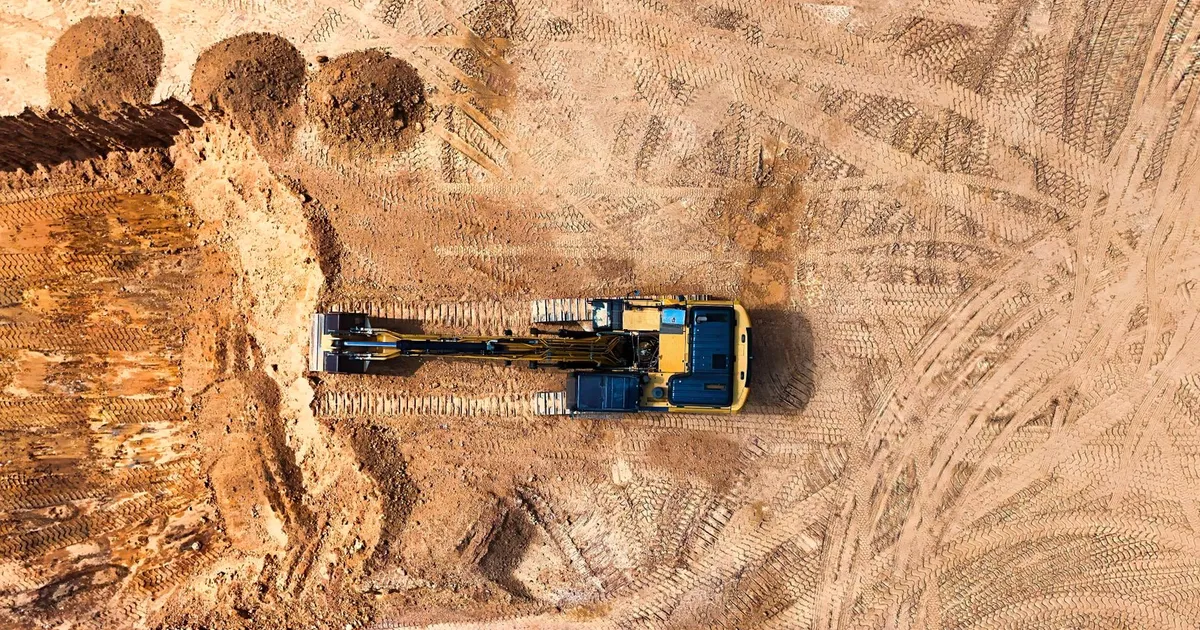Aerial photo of an excavator working on a large empty construction site.