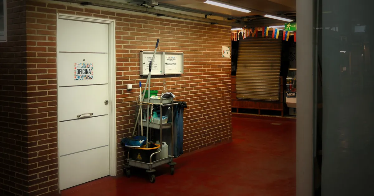 A brightly lit industrial hallway with a cleaning cart and supplies near an office door.