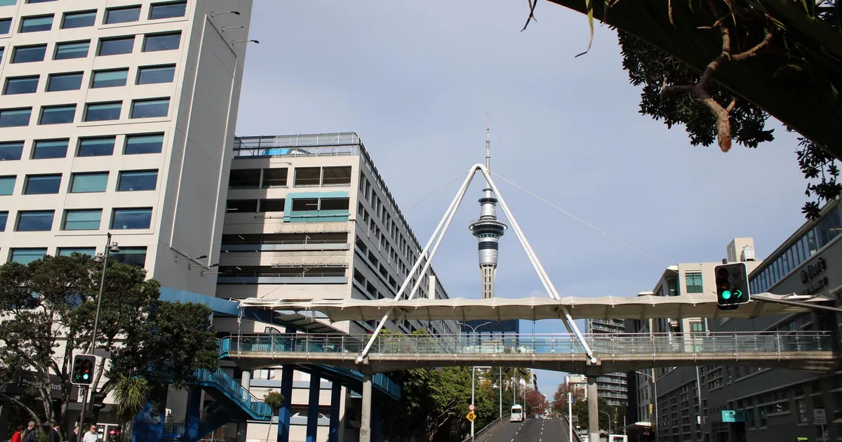 Urban scene featuring a pedestrian bridge and iconic Skytower in a bustling cityscape.