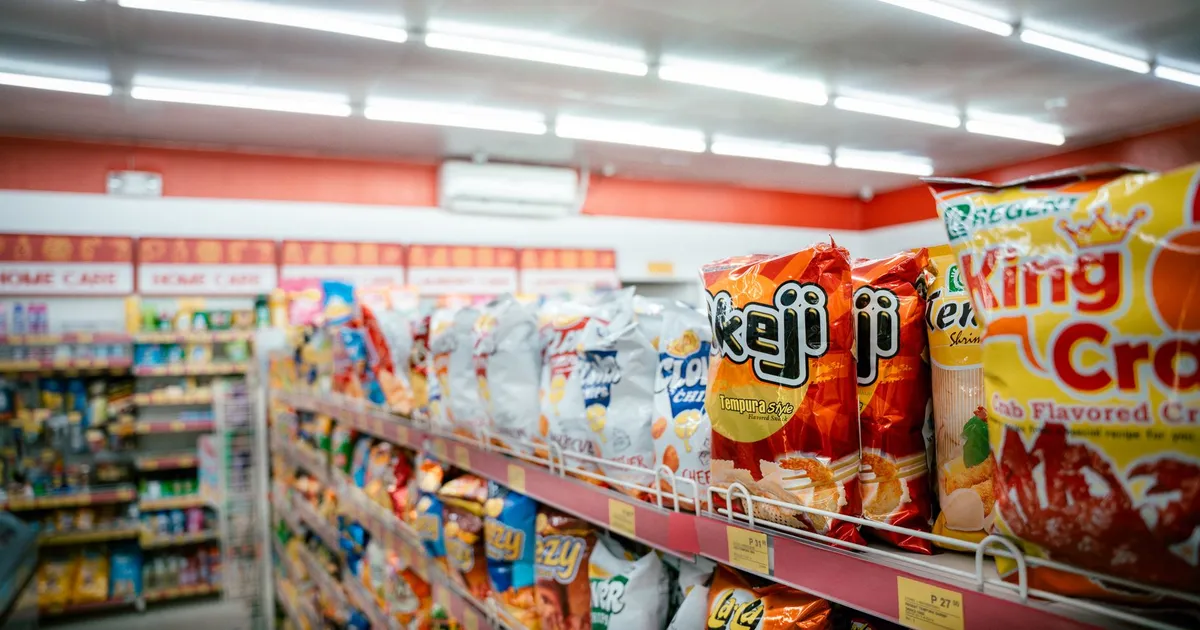 Wide shot of vibrant snack aisle in a supermarket with various chip bags on display.