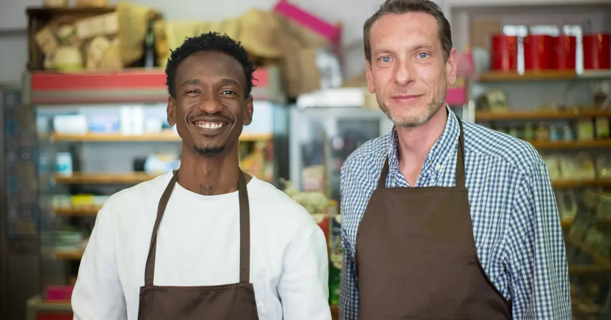 Two happy store owners smiling while wearing aprons in a local grocery store.