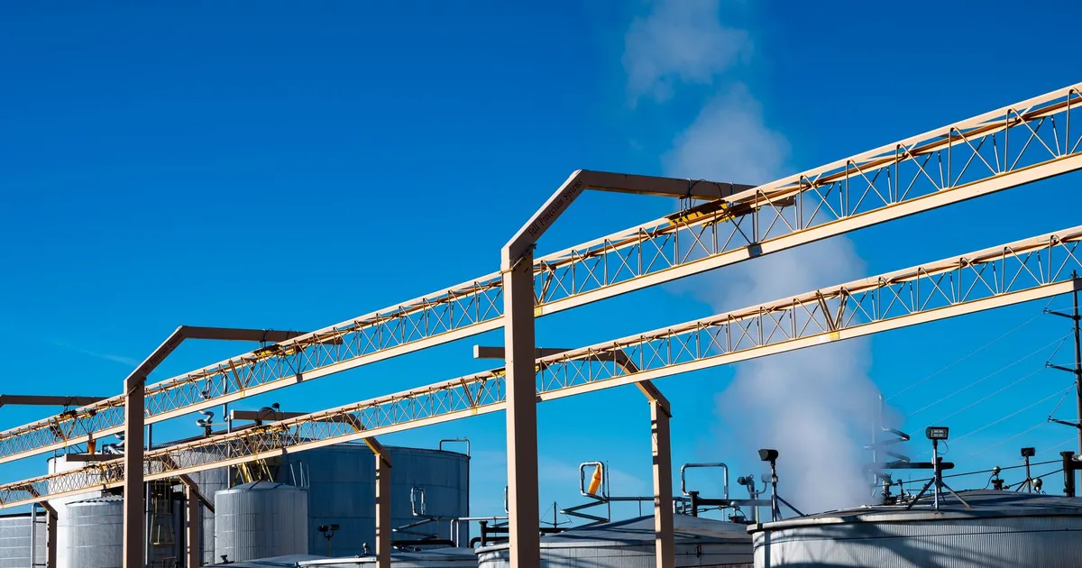 Wide view of an industrial plant with smoke rising from storage tanks against a clear blue sky.