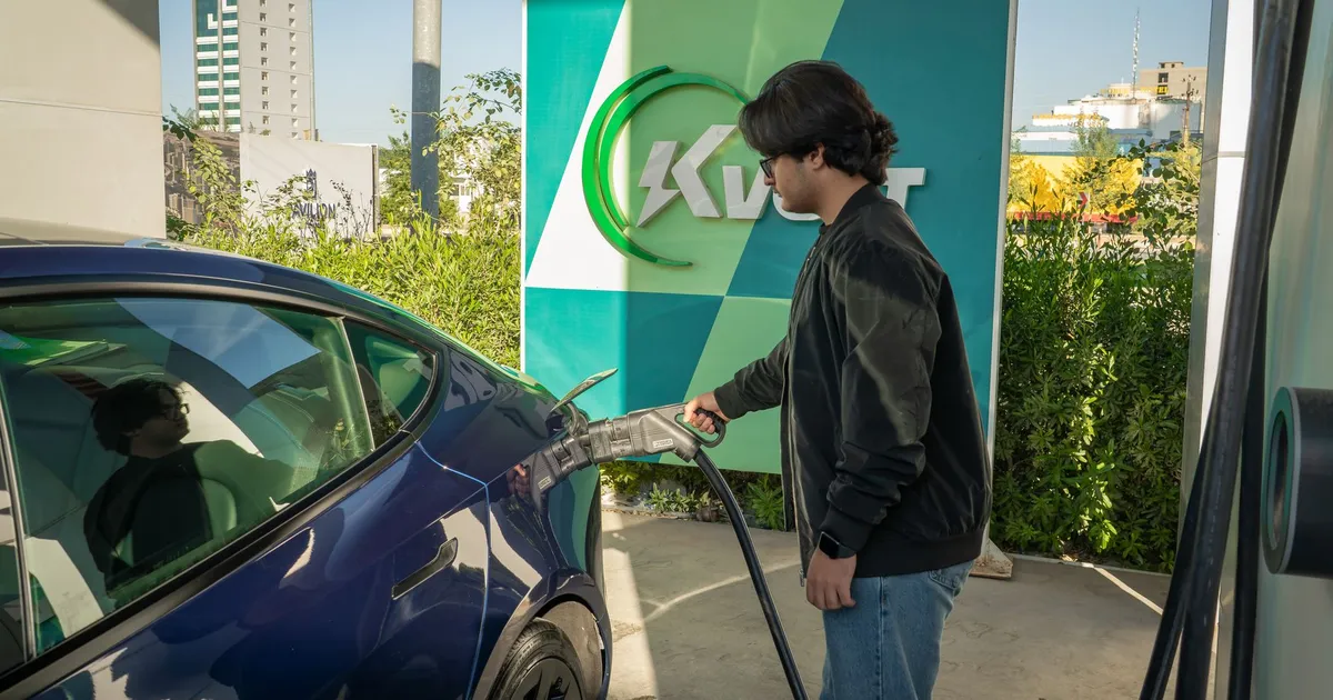 Young man charging a Tesla Model 3 at an outdoor electric vehicle station during the day.