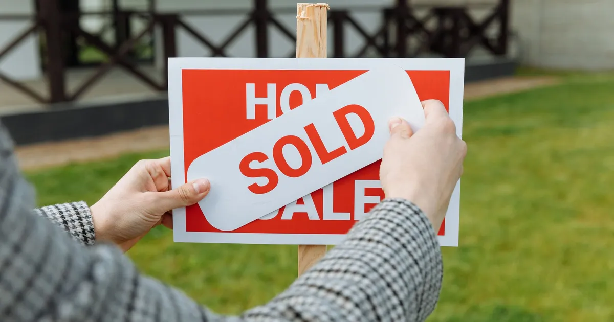 Close-up of hands placing a sold sticker on a real estate sign outside a house.