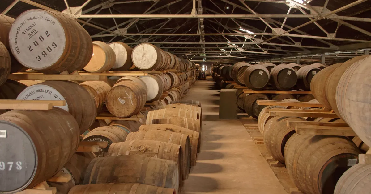 Rows of wooden barrels aging in a historic distillery warehouse, creating a rustic atmosphere.