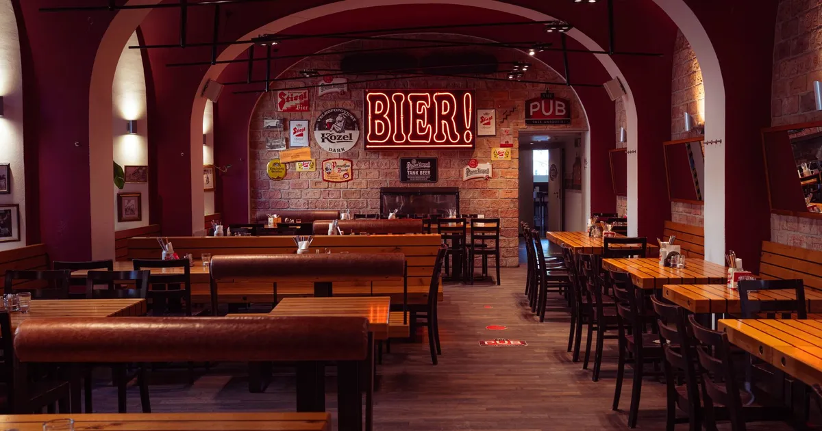 Empty European pub interior showcasing wooden tables, warm lighting, and vintage beer signs, creating a classic inviting ambiance.
