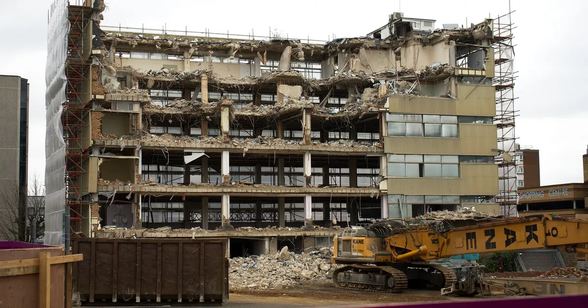 A multi-story building in England undergoing demolition, revealing exposed concrete and debris.