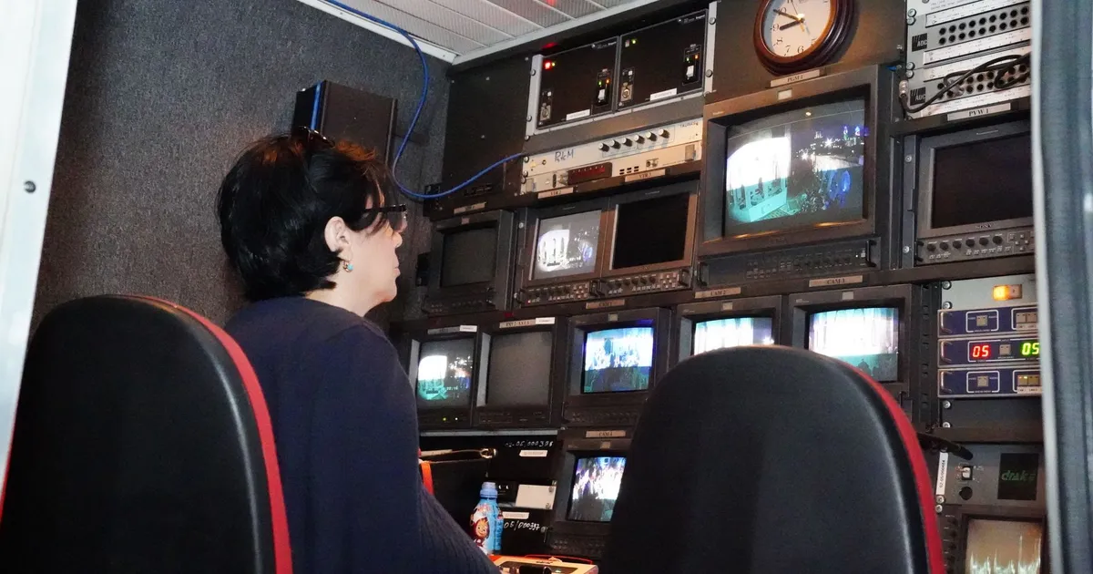 A professional in a TV broadcast control room with multiple screens and equipment.
