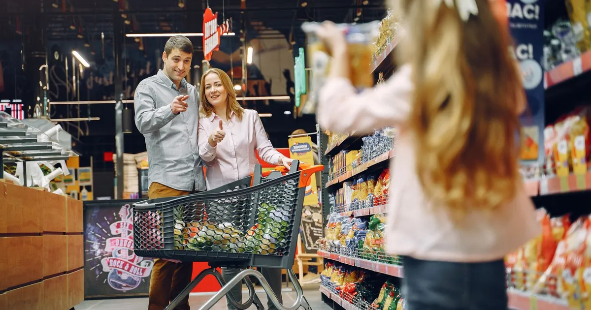 Happy family shopping in supermarket aisle with daughter holding snack box.