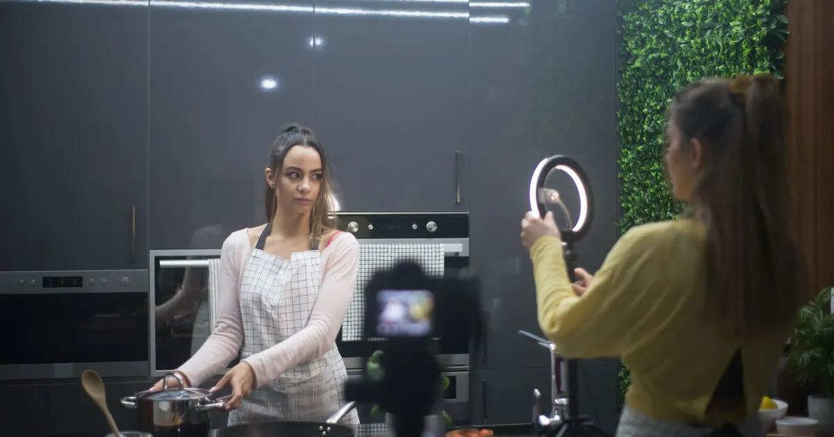 Two women creating a cooking video in a stylish kitchen setup with ring light.