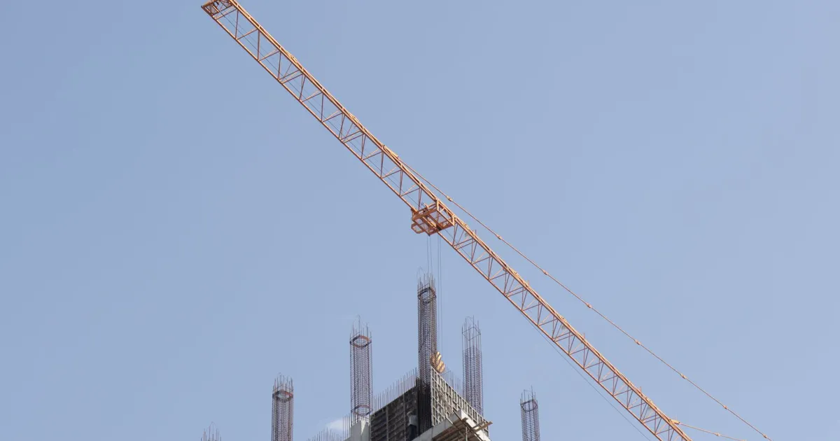 Tower crane working on a high-rise building construction site against a clear blue sky.