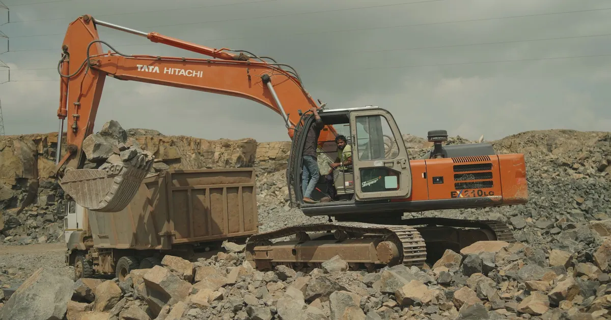 Excavator loading rocks into a dump truck at a quarry site, showcasing industrial equipment in action.