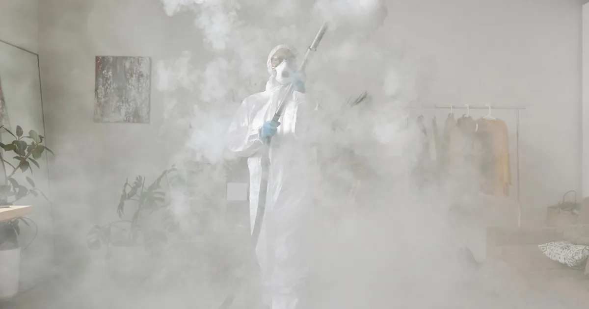 Person wearing PPE suit fogging a room for disinfection. Indoor safety measures.