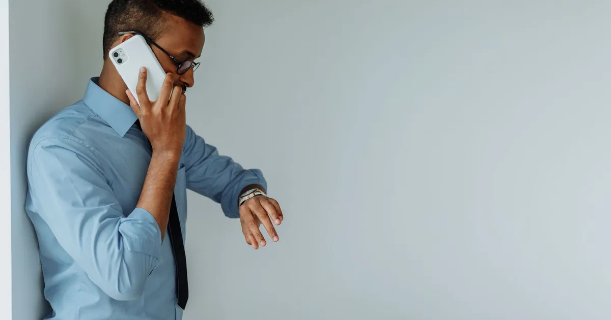 Professional man in office attire checking time on wristwatch while on phone call indoors.