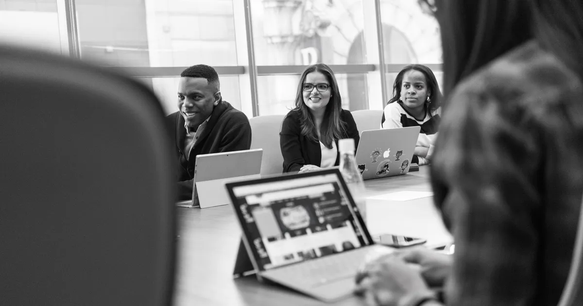 Diverse team of adults engaged in a meeting using laptops in a modern office setting.