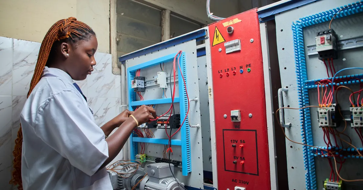 Young female technician repairing electrical control panel in industrial setting.