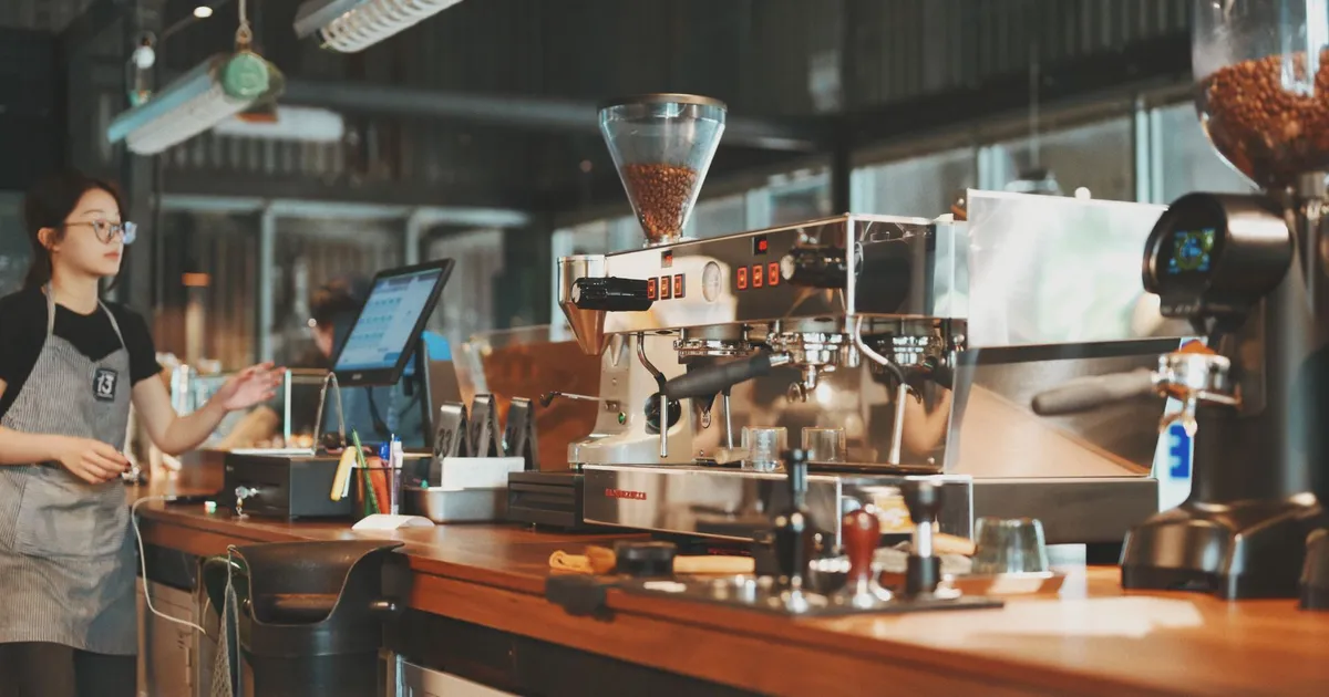 Barista at coffee shop counter using espresso machine for fresh brew coffee.