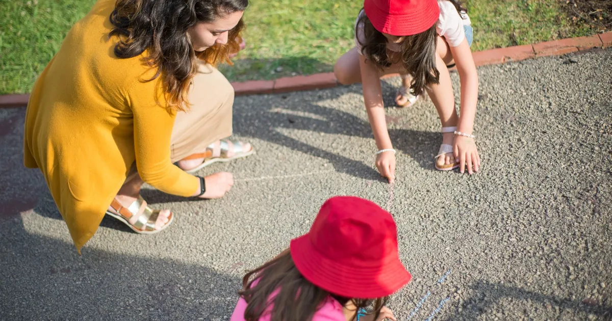 A nanny and two children drawing together on the pavement outdoors in Portugal.