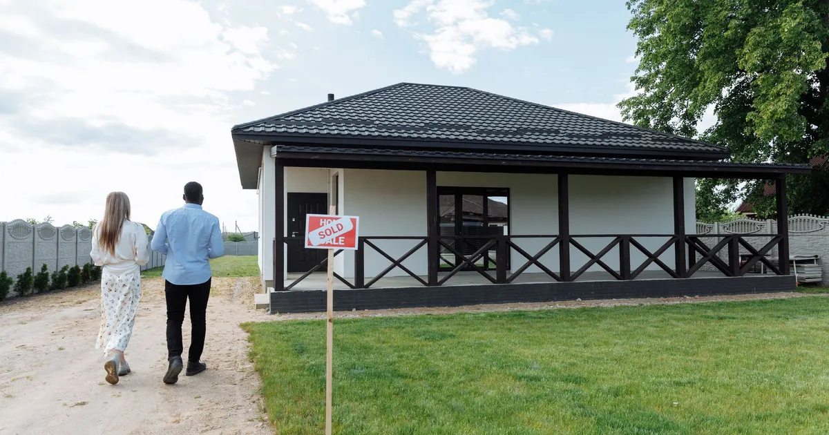 A couple walks towards their newly purchased home; a sign indicates the house is sold.
