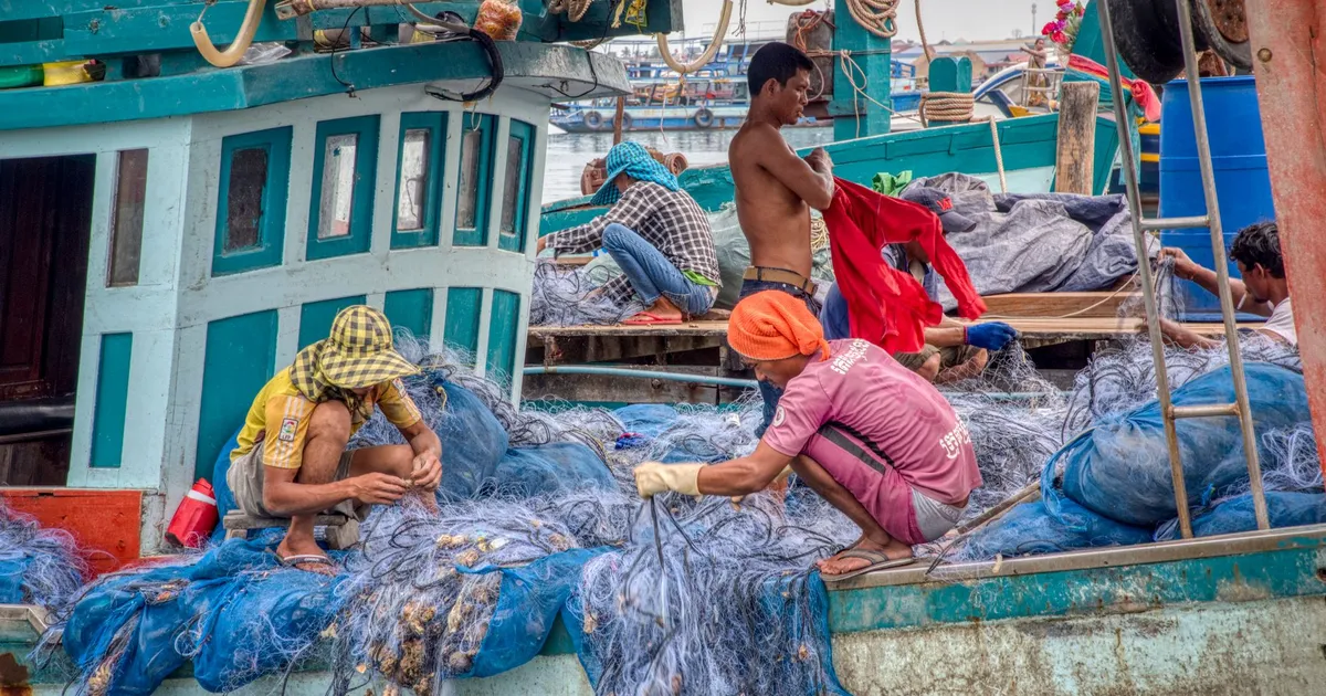 Fishermen repairing nets on a traditional trawler, highlighting maritime livelihood and culture.