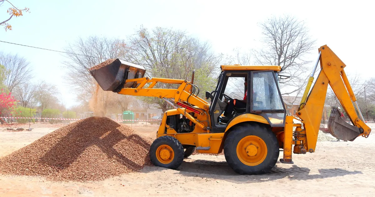 A yellow excavator moving gravel at an outdoor construction site during the day with clear skies.
