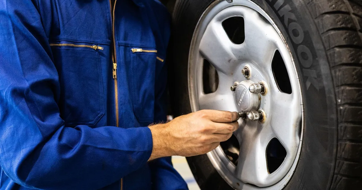 Mechanic in blue coveralls inspecting a car tire in an auto repair workshop.