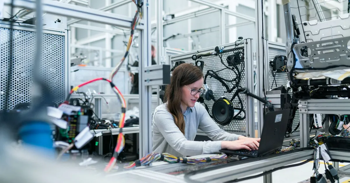 A female engineer focuses on her laptop amidst advanced tech equipment in a lab.
