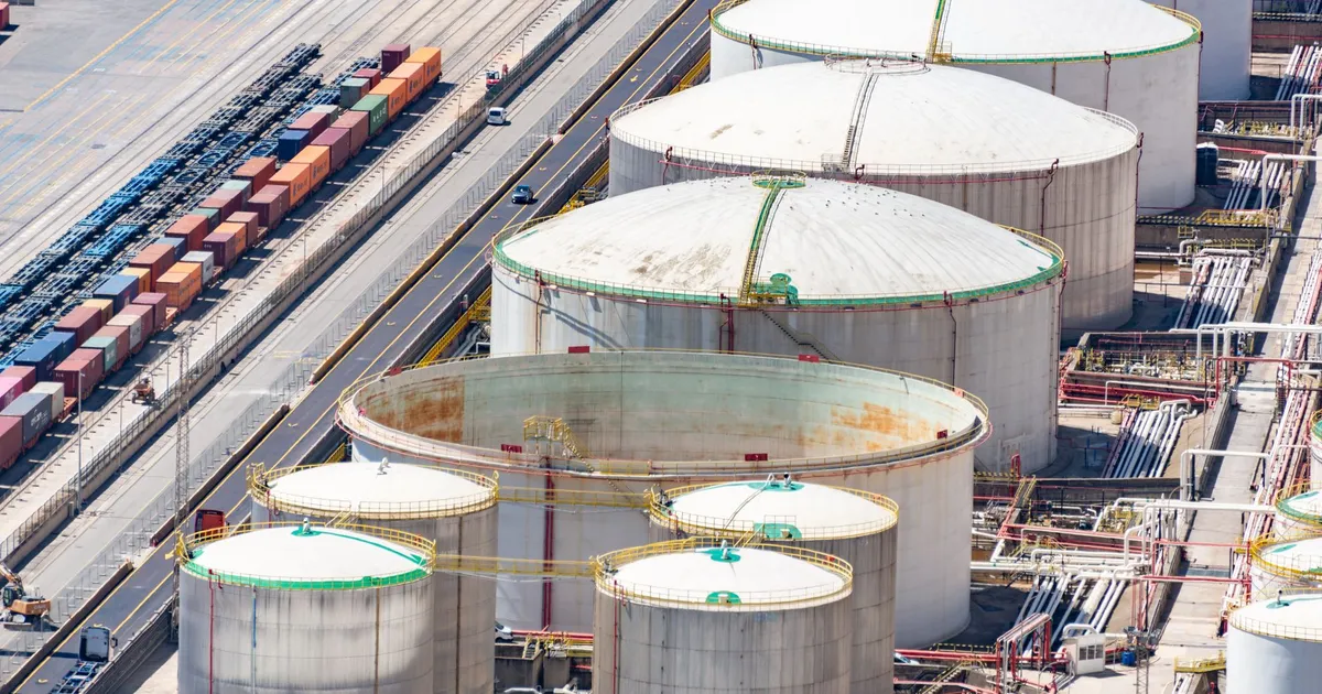 Aerial shot of large oil storage tanks in an industrial district with adjacent railway tracks.
