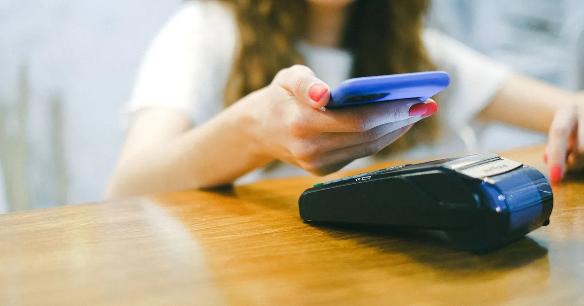A woman processes a contactless payment using her smartphone at a payment terminal.