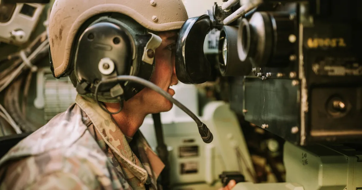 A soldier in uniform operates military equipment inside a vehicle, showcasing modern military technology.