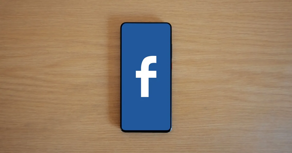 Smartphone with Facebook logo on screen, placed on a wooden background. Top view.