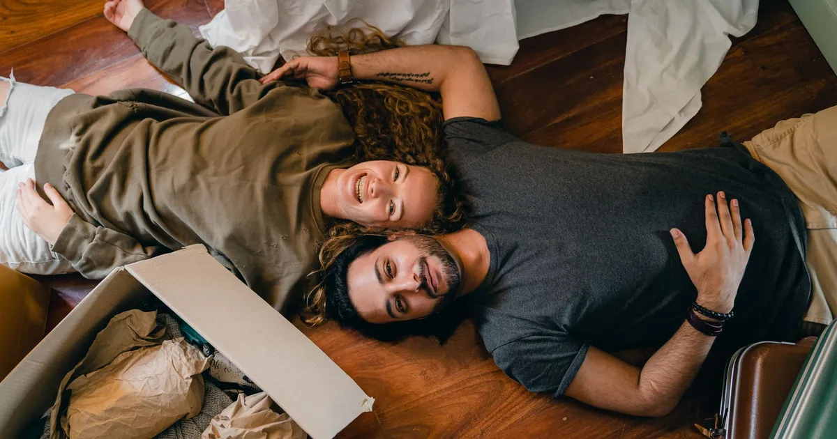 From above of young smiling diverse couple in casual clothing relaxing on floor near carton boxes while unpacking belongings in new contemporary apartment
