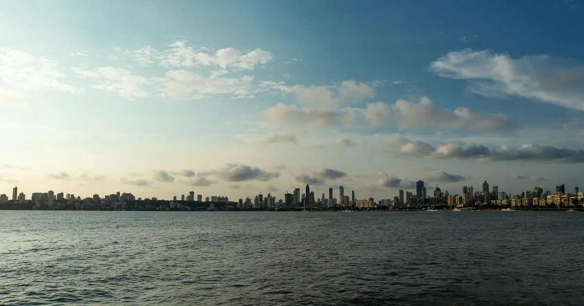 Panoramic view of Mumbai skyline with calm sea and cloudy sky in daylight.