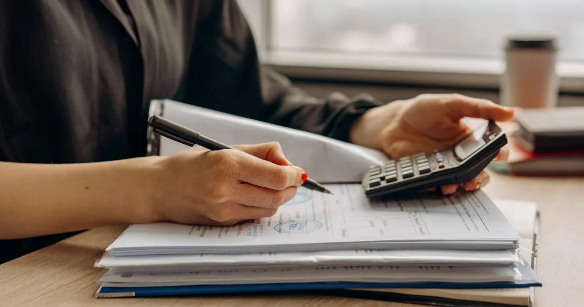 Close-up of person using a calculator with financial documents in an office.