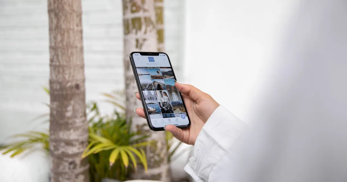A woman using a smartphone to browse social media while standing outdoors in a tropical setting.