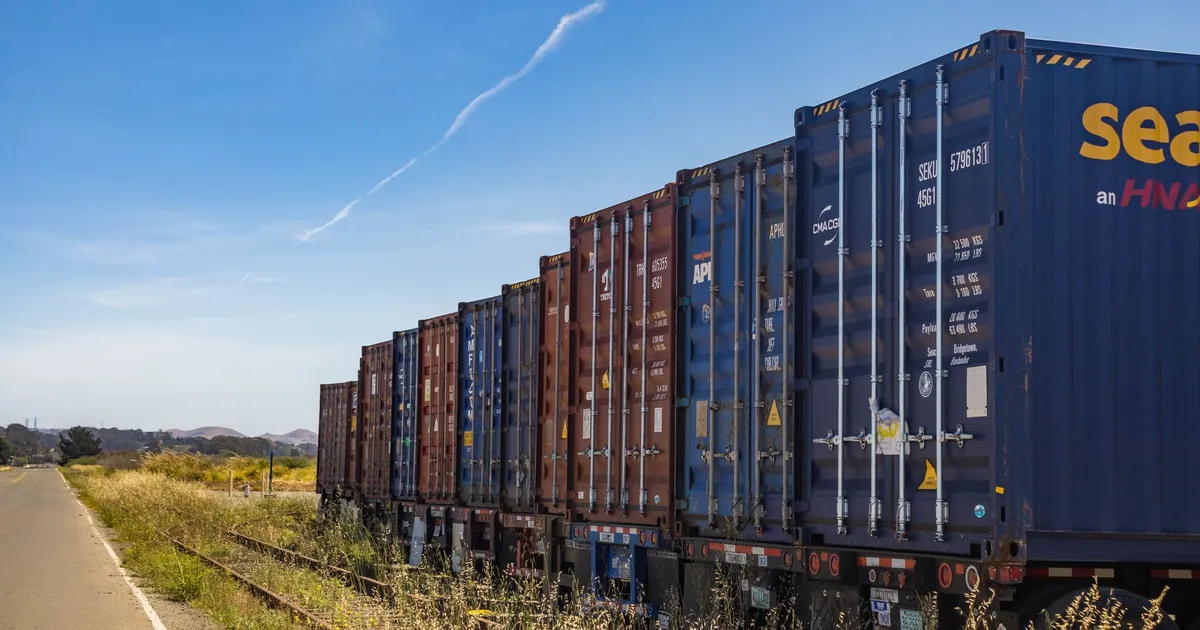 Colorful cargo containers on a freight train along a rural railway track under a clear blue sky.