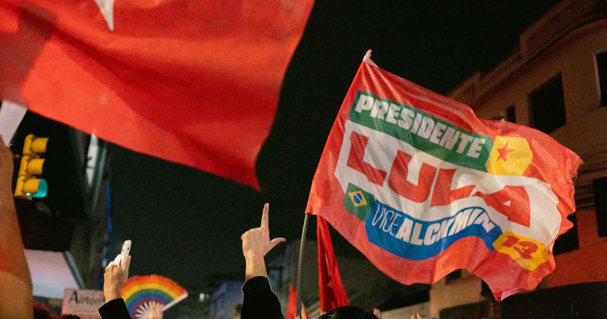 Supporters at a night rally waving flags with political slogans and hand signs.