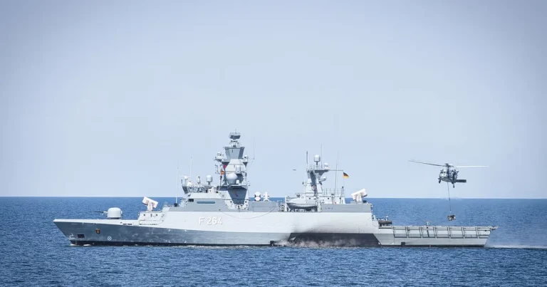 A naval frigate navigates open waters with a hovering helicopter, showcasing maritime operations.