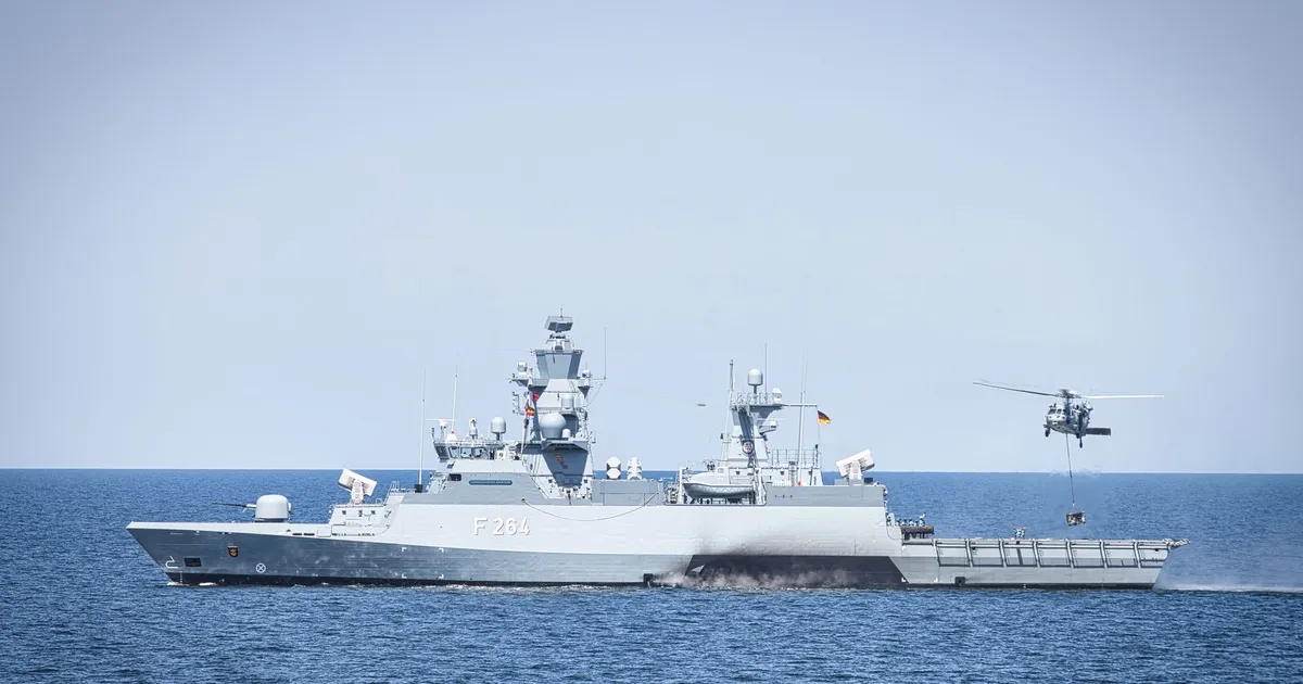 A naval frigate navigates open waters with a hovering helicopter, showcasing maritime operations.