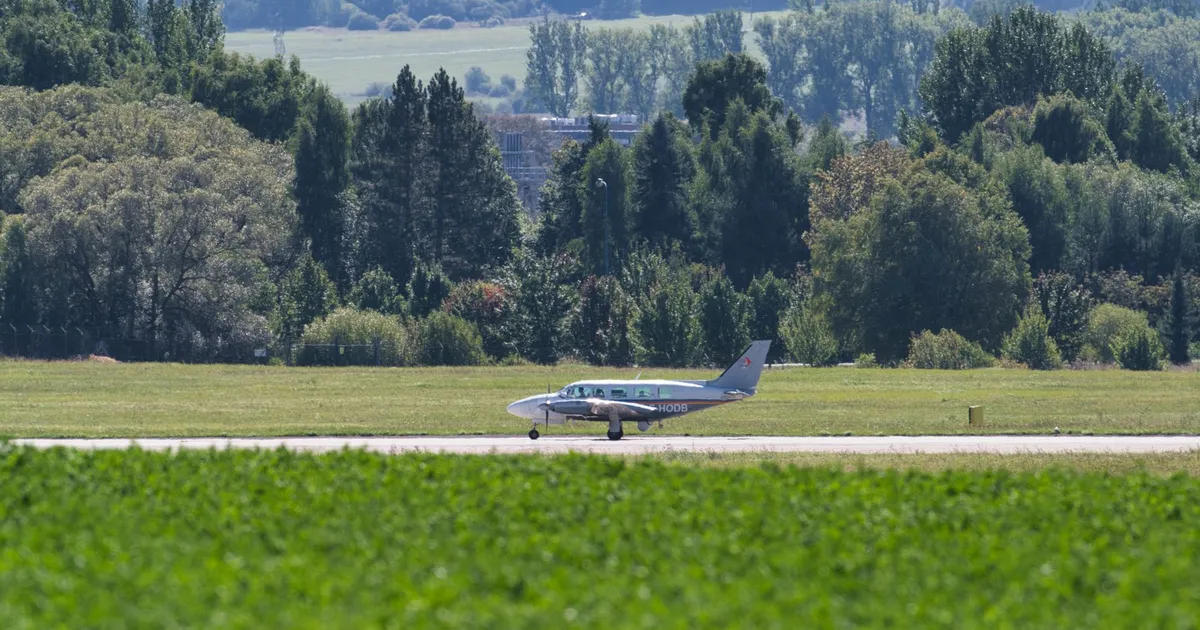 Small propeller aircraft on runway in lush forested landscape, Poprad, Slovakia.