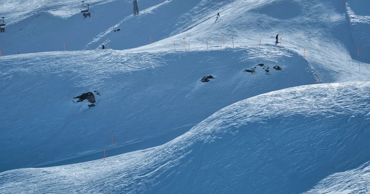 Scenic view of a snowy ski resort slope with skiers and chairlifts under a clear winter sky.