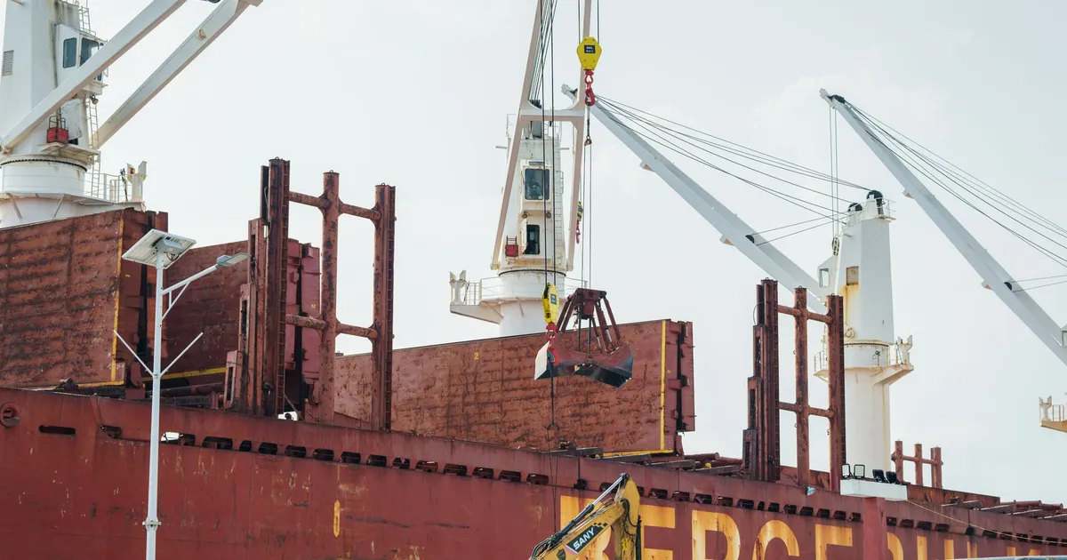 A large cargo ship at a port with cranes lifting containers on a clear day.