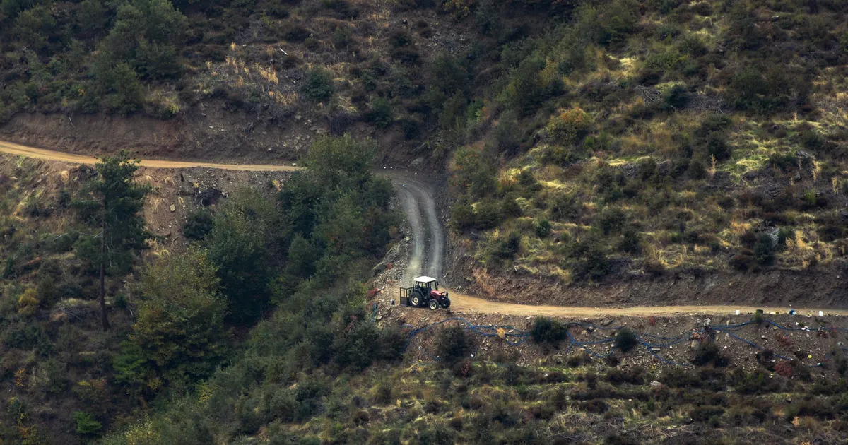 A solitary tractor navigating a winding dirt road through rugged mountain terrain.