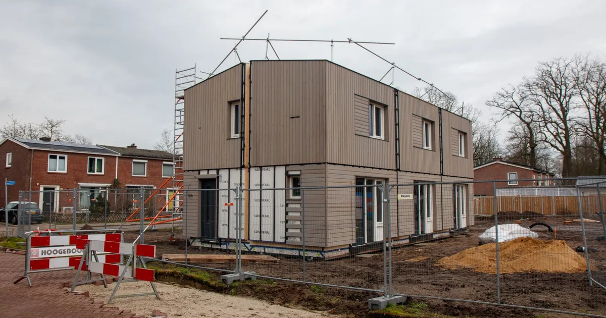 A modern house under construction with scaffolding, fences, and construction signs on a cloudy day.