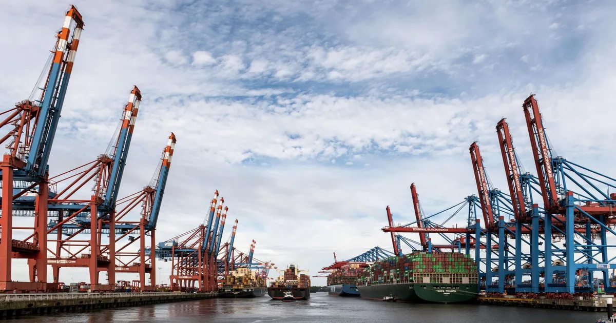 Wide view of container ships and cranes at Hamburg port under a cloudy sky.