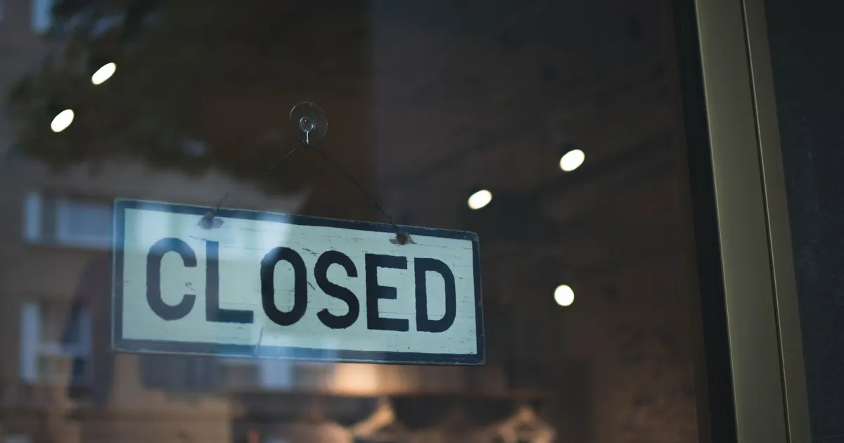 A closed sign hangs on a glass window of a modern urban storefront.