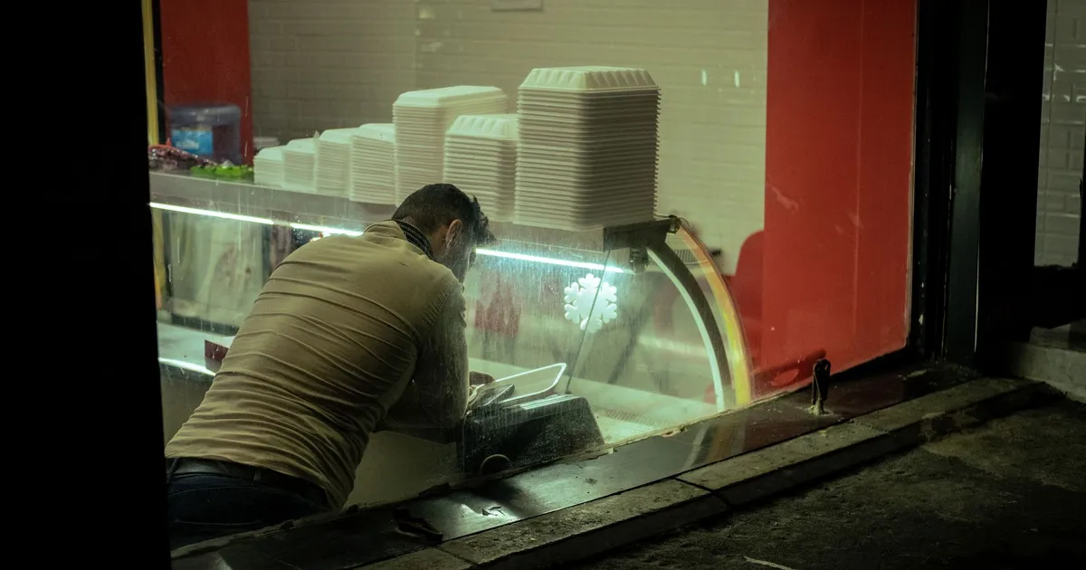 A man arranging containers in a takeaway restaurant, seen through a window.