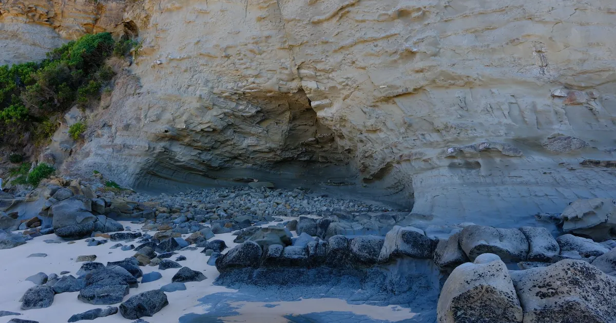 Explore the rugged beauty of a rocky coastal cliff face with scattered stones and sandy shore.